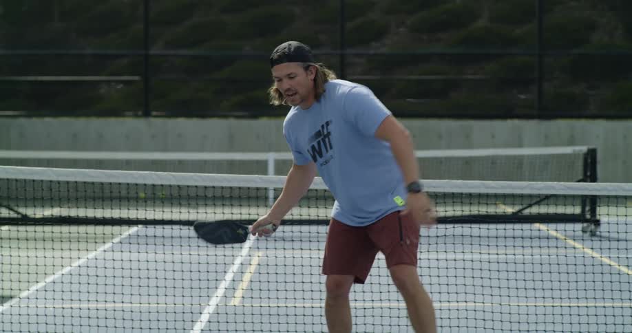 A man in a tshirt and shorts plays tennis on an outdoor court