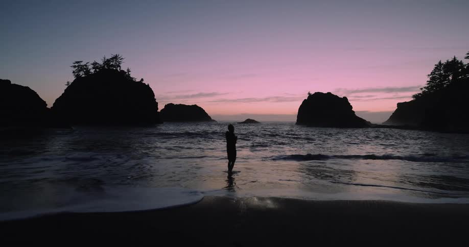 Silhouette of a boy walking around the coastline on a beach next to promontories at evening