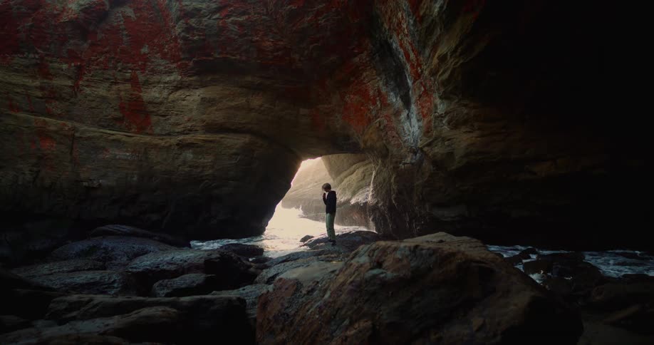 Young man stands inside a large cavern on the coast at daytime