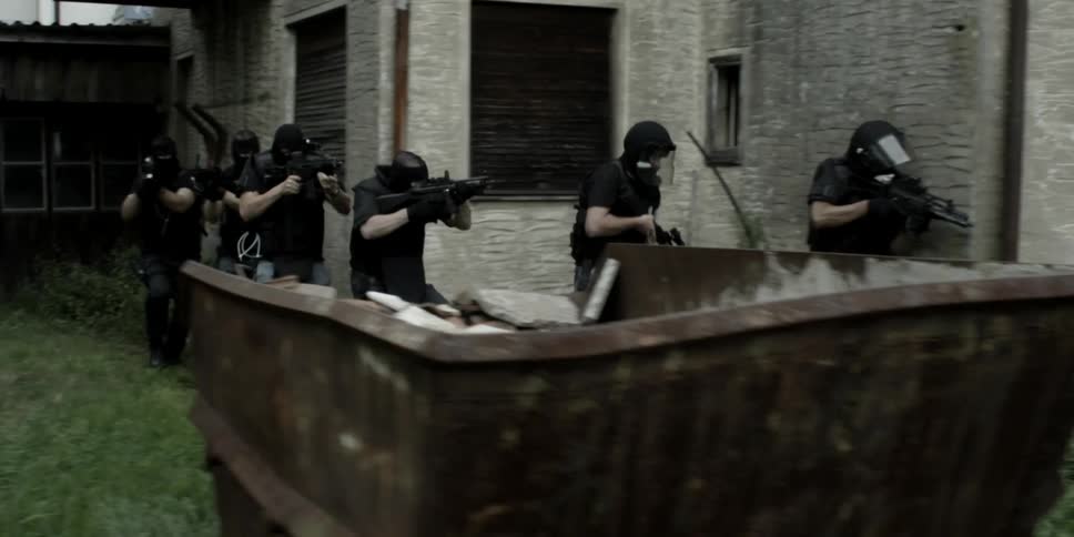 A group of armed men walk around a house
