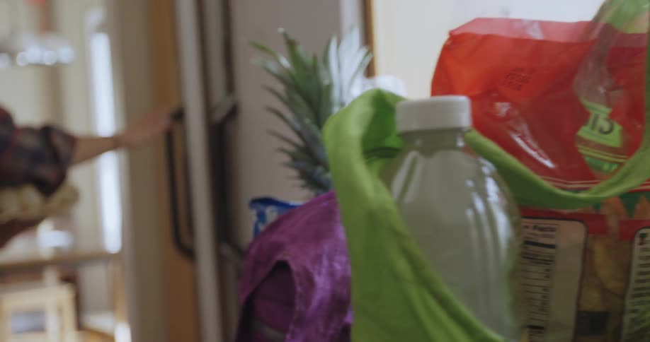 A woman pulls items out of a refrigerator and puts them into grocery totes