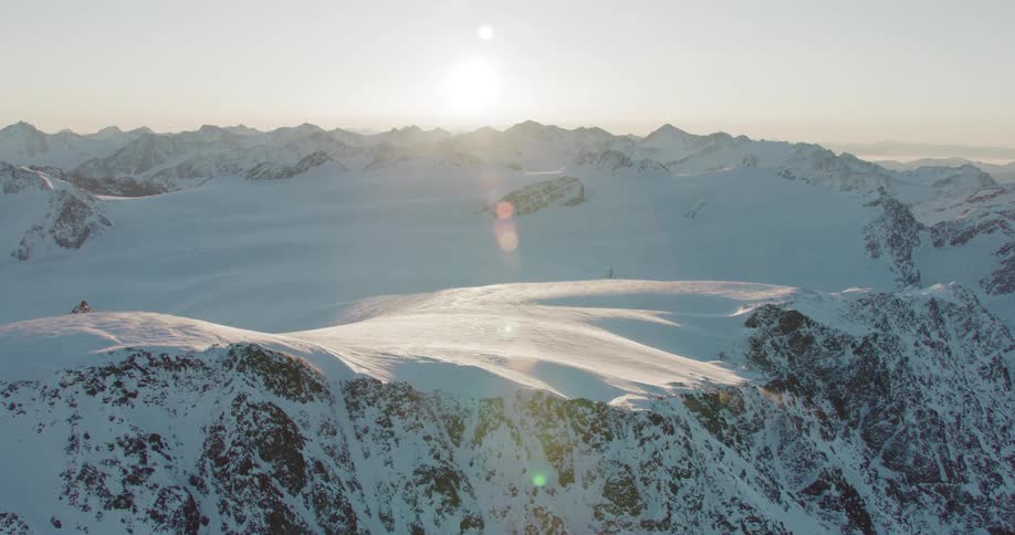 An aerial of snow covered mountain ridges with the sun on the horizon