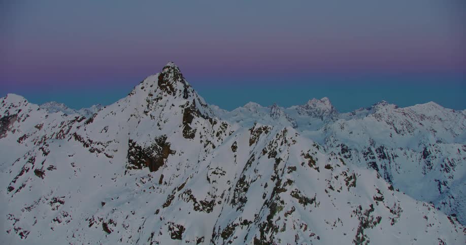 Snow covered mountains with peaks high in a clear colorful sky