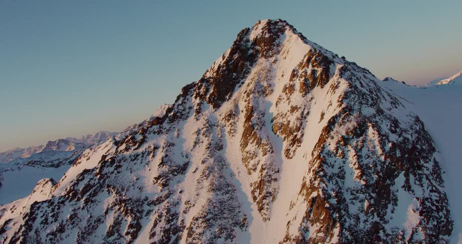 The sun shines on the rough terrain of snow covered mountains with peaks high in a clear sky