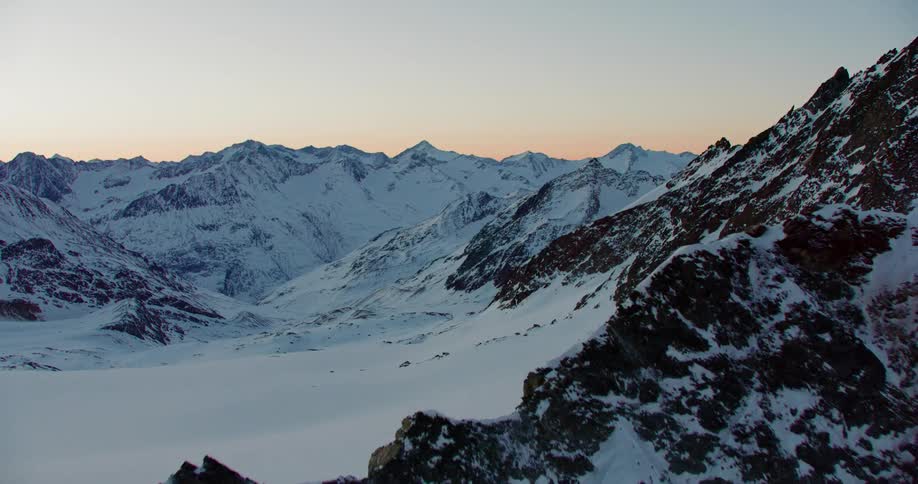 Moving over snow covered mountains with peaks in a clear blue sky
