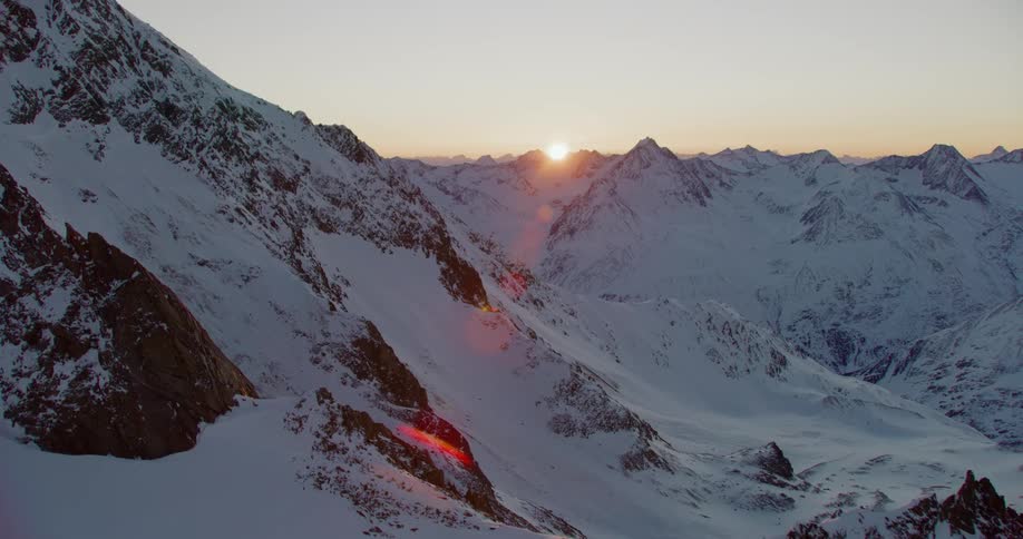 The sun barely peaks over a snow covered mountain range in the distance