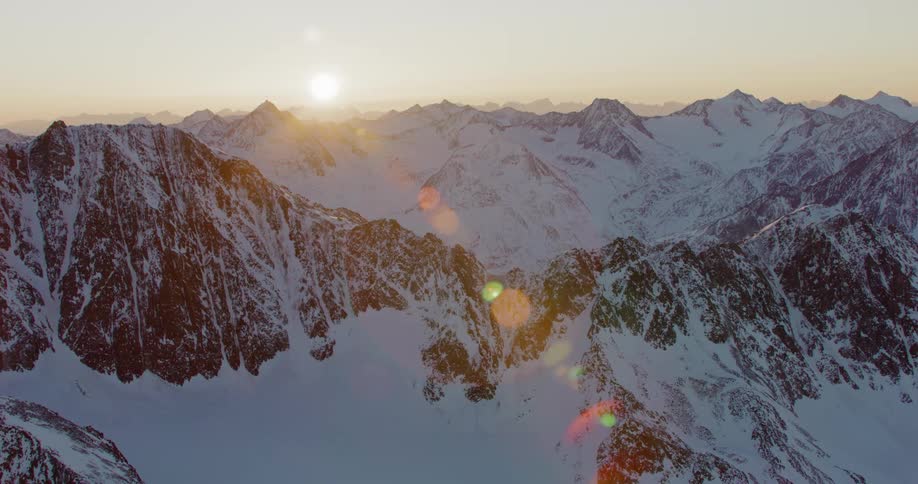 A low sun hangs in the sky over a snowy mountain range