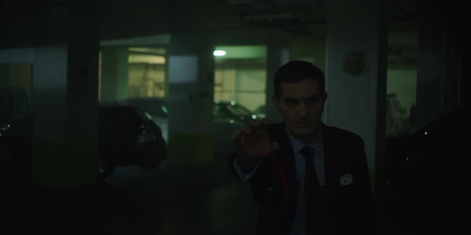A man is walking oddly through a parking garage at night