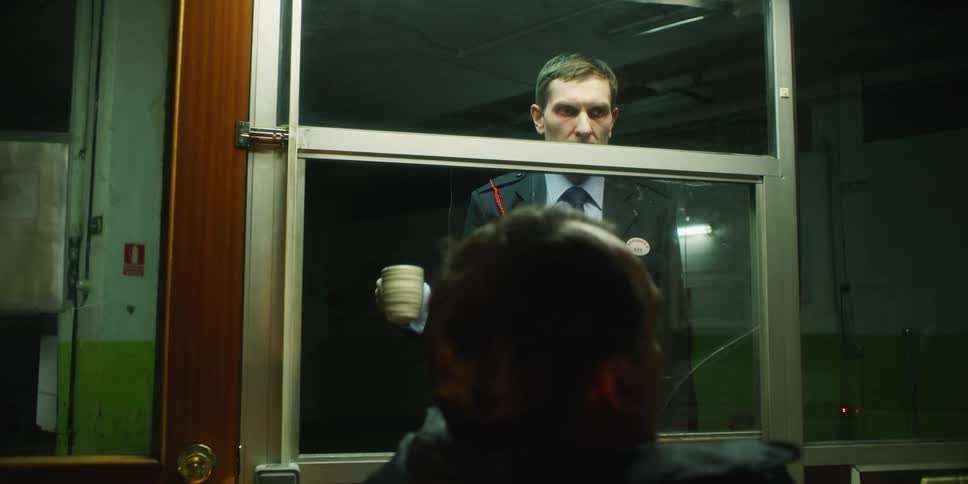 Man pounds on a window and takes a mug from the man on the other side