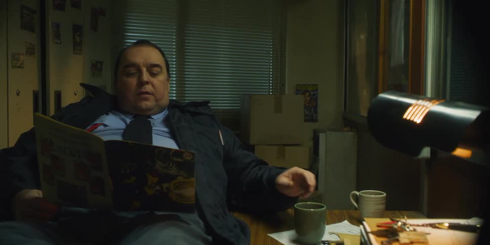Man reads a magazine and drinks from a mug as he sits near a desk
