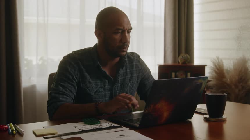 Man makes marks on house design while sitting in office and using a laptop