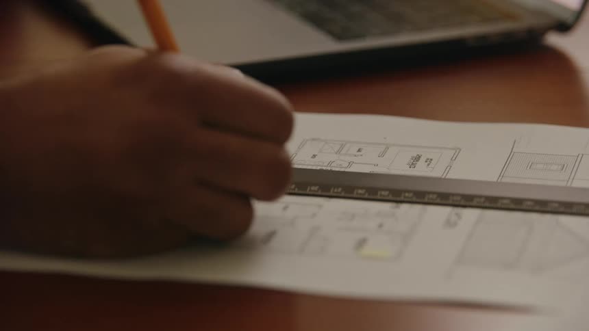 Man consults floor plans on laptop and writes on printed floor plan