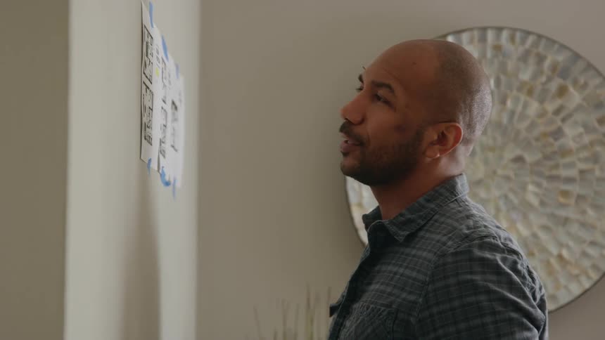 A man is standing near the wall holding a calculator and looking at a chart and looks up across the ceiling
