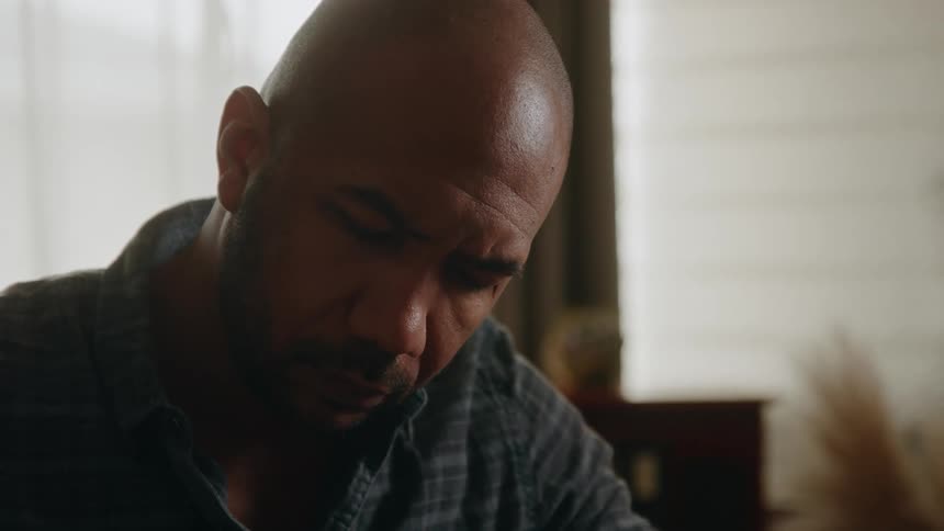 A bald man writes and pauses to think about his writing