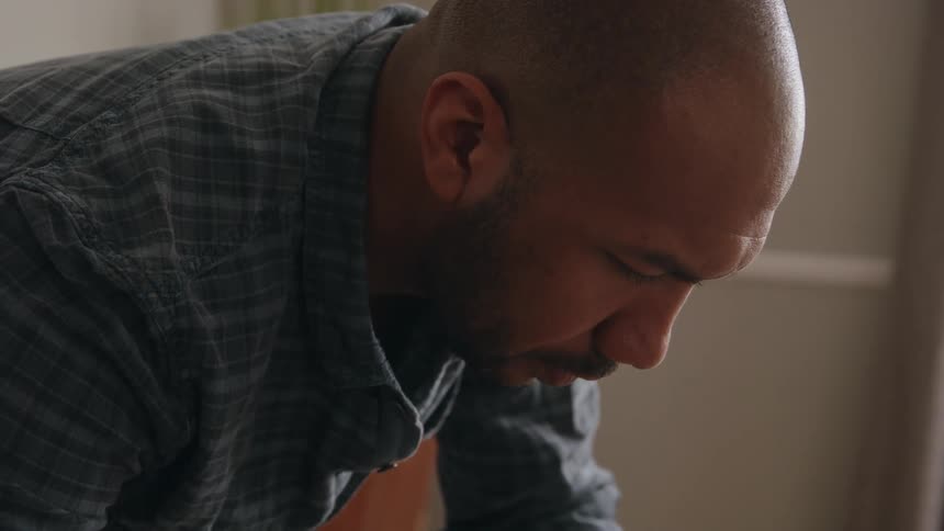 A man is leaning over with a pencil in his hand as he looks at charts on a table with pens and a calculator