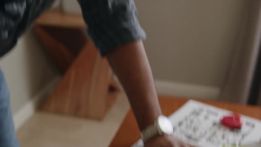 A man leaned over on a table while he writes with a pencil on papers on the desk