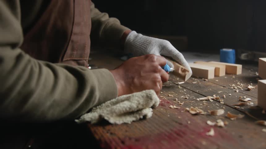 A man holds up a piece of wood as he is carving using a blade