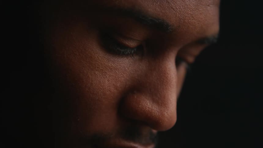 Light shines on the face of a man looking down and appears to be in deep thought