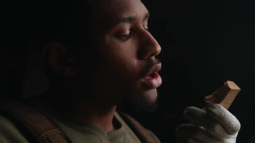 A young man inspects and blows on a small block of wood