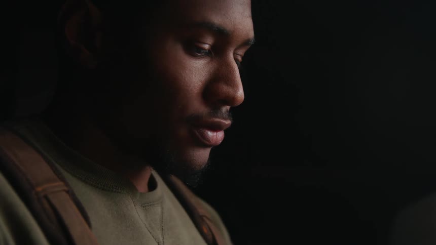 Light shines on a mans face as he looks down at something as he stands in a dark room