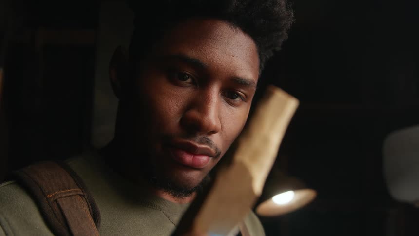 Man examines shaped piece of wood while standing in dim workshop