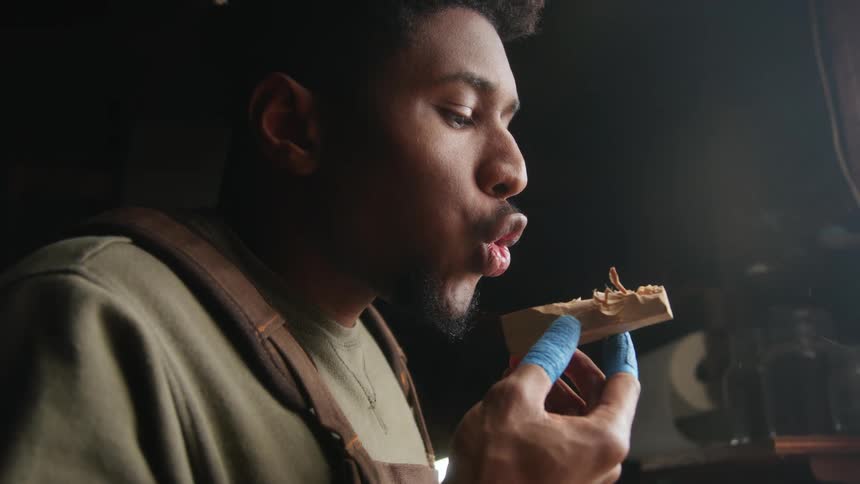 A mans face as he blows dust off a small wood piece in his hands