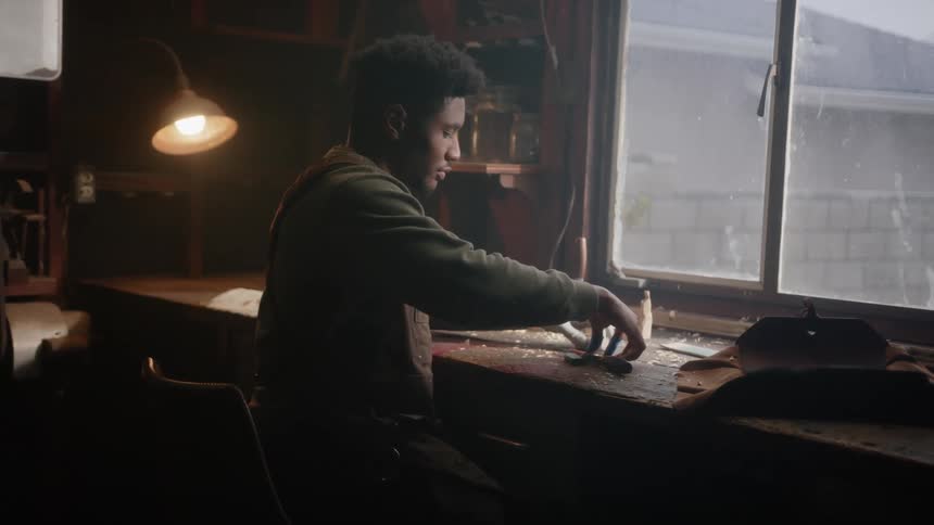 Man sits at workbench carving wood near window