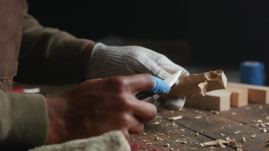 Close up of the hands of a carpenter carving a small piece of wood with a knife in the workshop