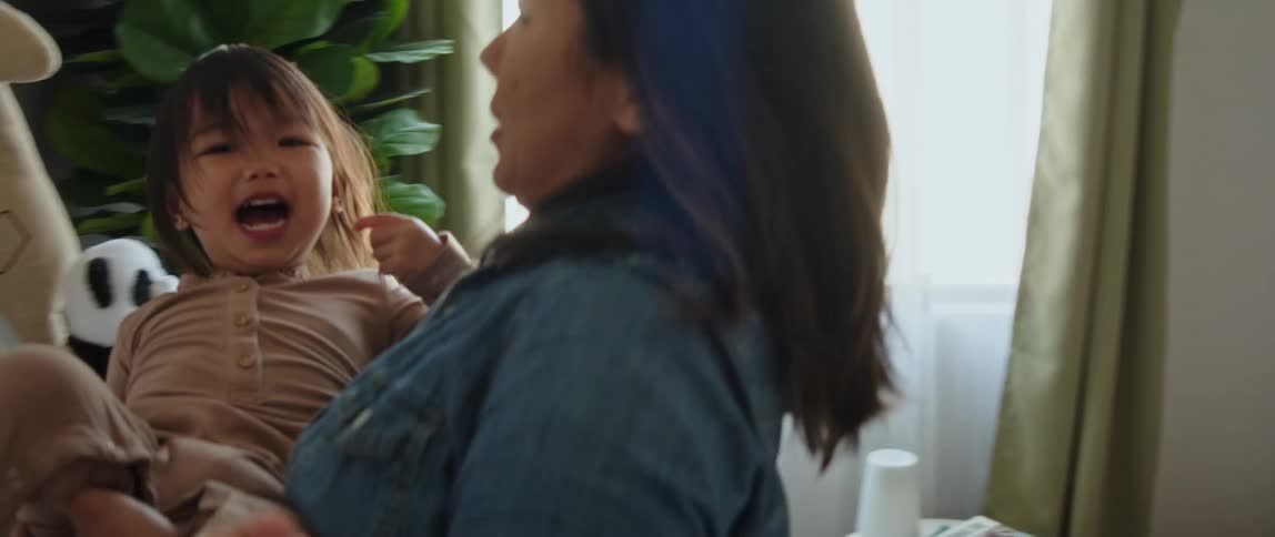 Mother carries her daughter from the crib to the changing station in her room