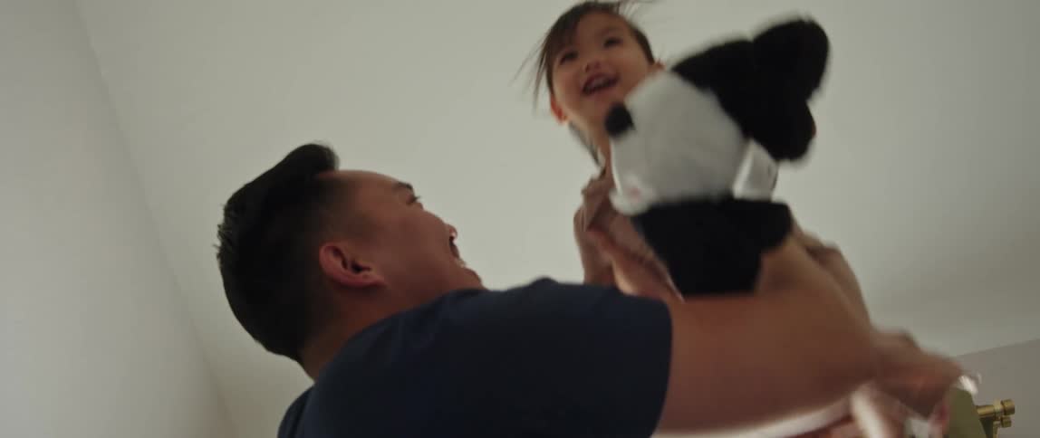 A father lifts his daughter up in the air and kisses her on the cheek