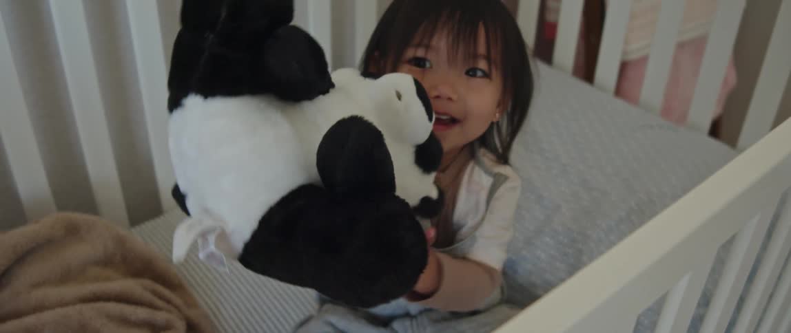Happy girl playing with her panda plush toy inside the crib