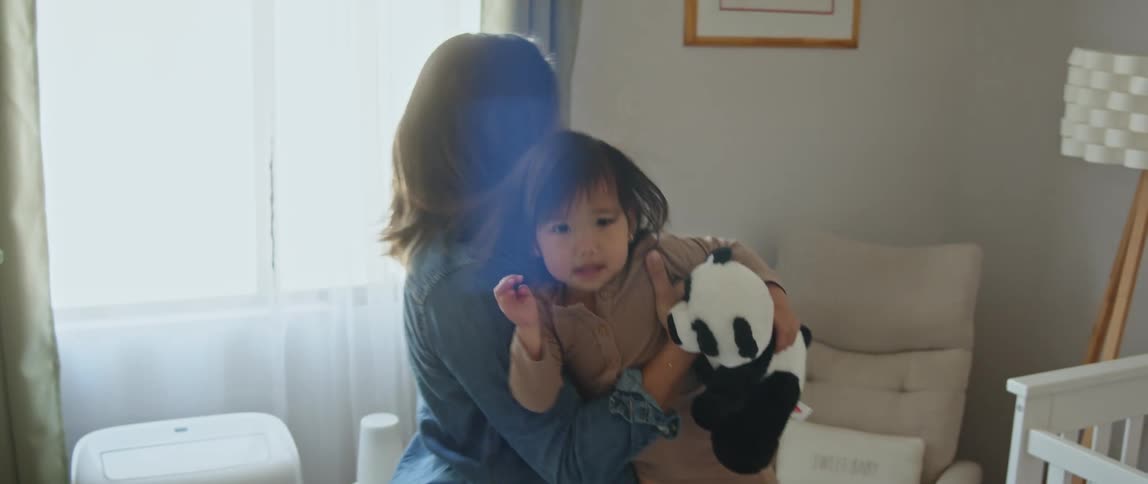 A mother picking up her daughter from the changing table and sitting in a chair in the corner with the girl on her lap