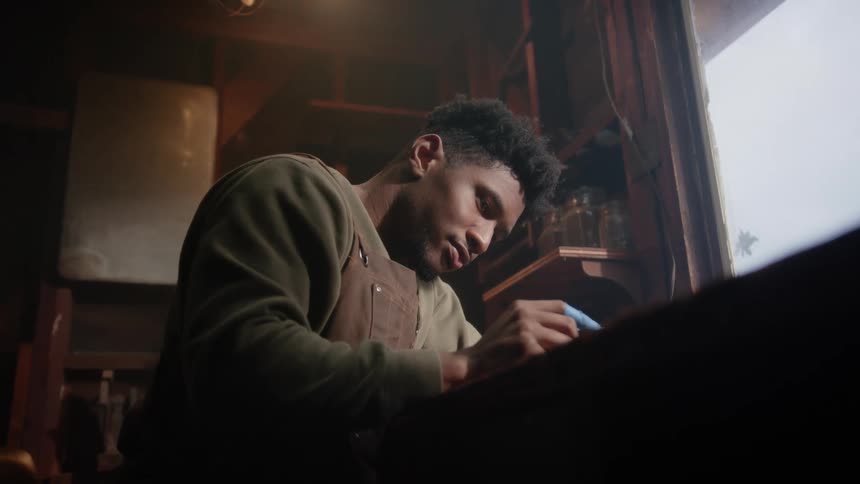 A young man holds up a piece of wood that he is carving using a small blade
