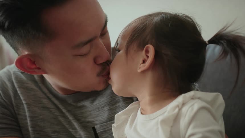 Father smiles wile exchanging a kiss with his daughter as they sit on couch