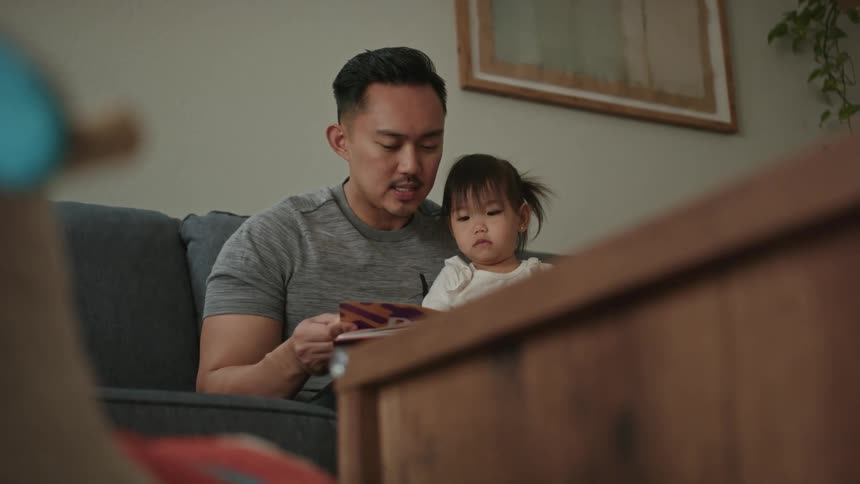 Father holds daughter on his lap while reading a book to her
