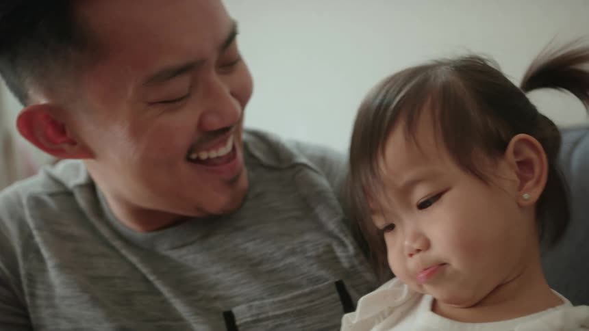 Daughter kisses father sitting on the couch laughing in the living room