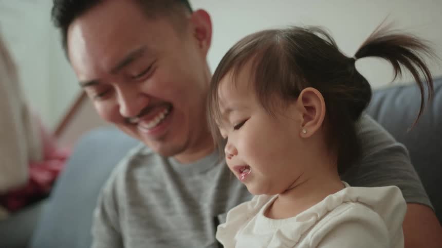A toddler girl sitting on her fathers lap as they smile and laugh and play