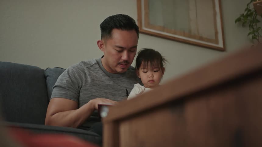 Father holds his daughter in his lap and reads her a book