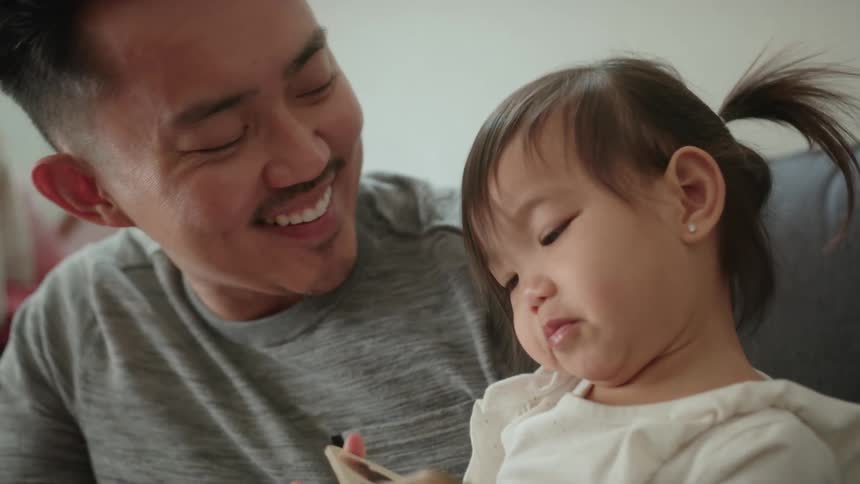 Daughter playing with chunky book exchanges cheek kisses with father
