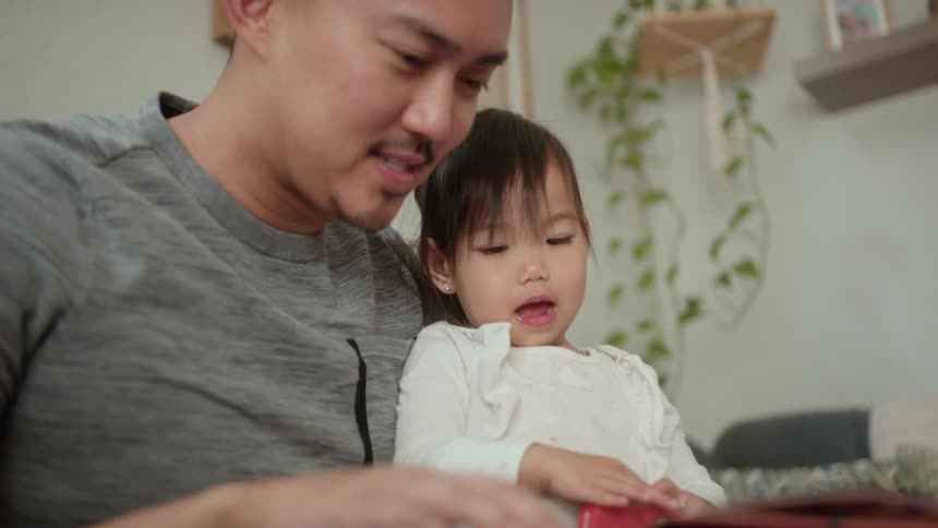 Father holds daughter on his lap while reading her a book