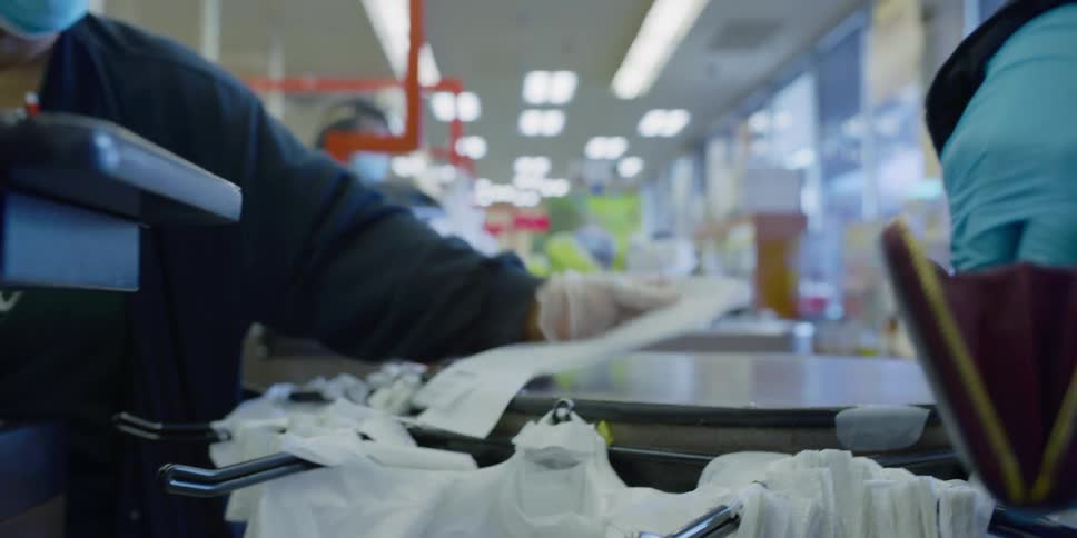 A woman with blue disposable gloves receiving change from a cashier then putting it in her purse