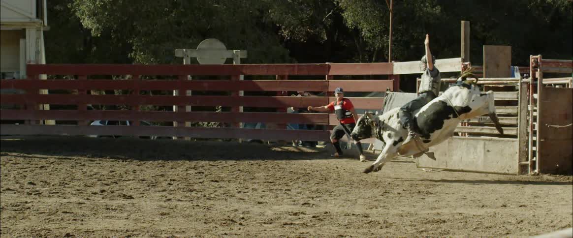 Man opens a gate with a rope to let out a man riding a bull