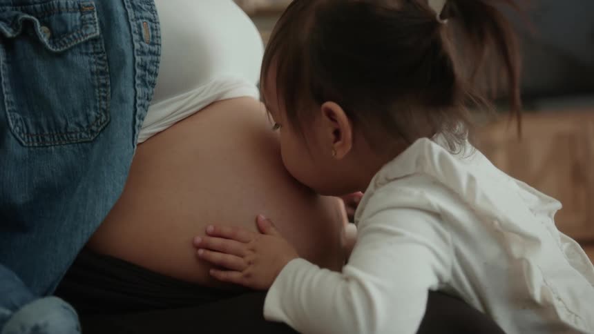 Toddler daughter kisses pregnant mothers belly in the living room