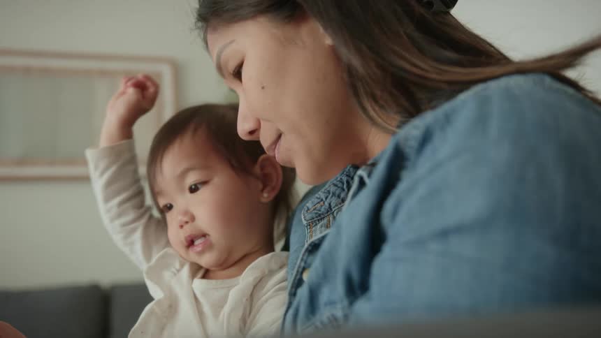 A mother and daughter sitting on a couch looking at a book as the child and mother smile and laugh