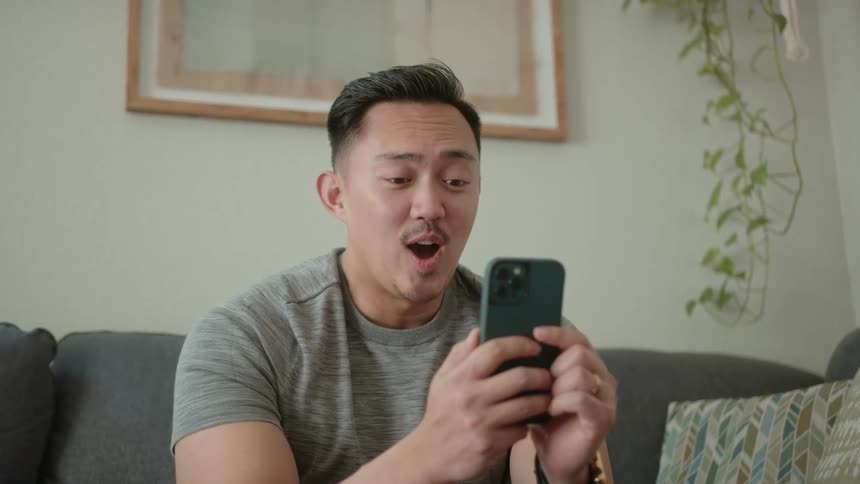 A young man is filming a video on his smartphone and he is smiling