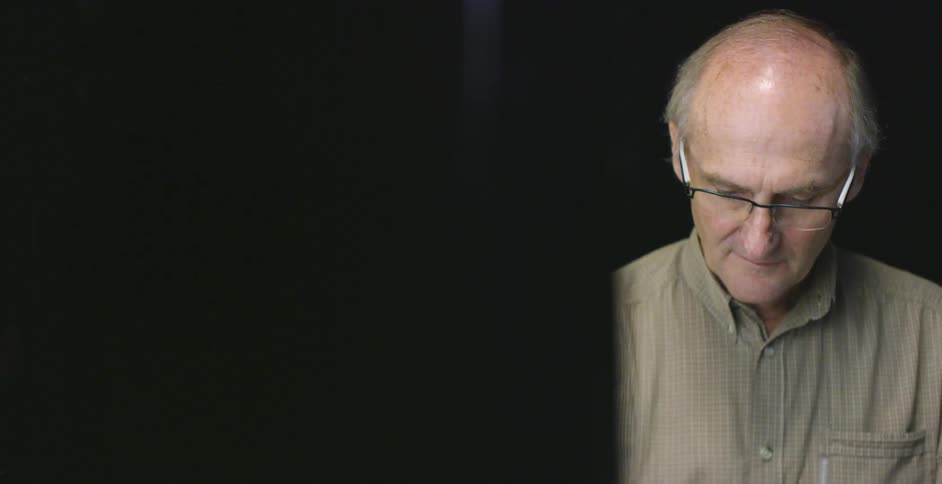 A bald man in glasses is looking down