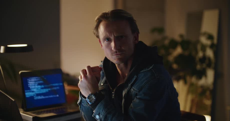 A man sits at his desk while lines of code flash on his computer