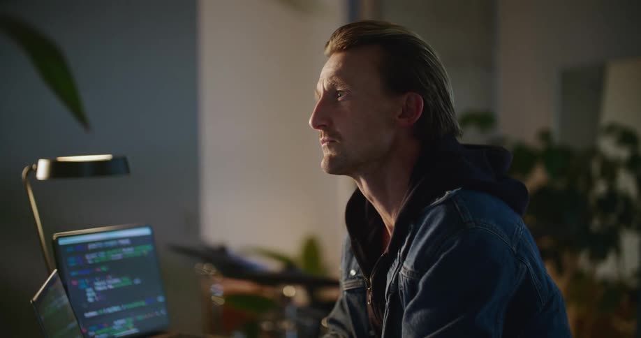 Man sits at desk with two computers and types on laptop