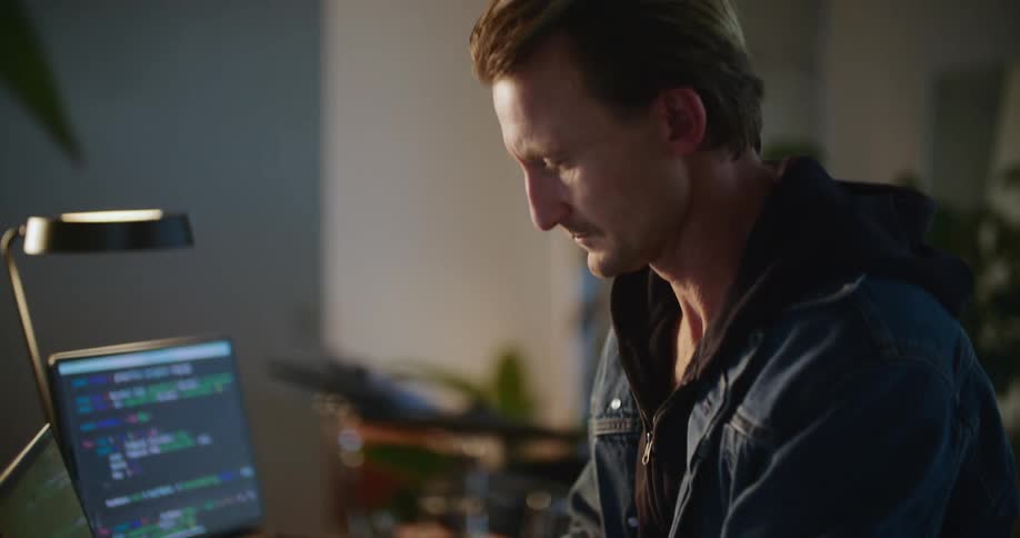 A man sits at his desk in his office and types on his laptop