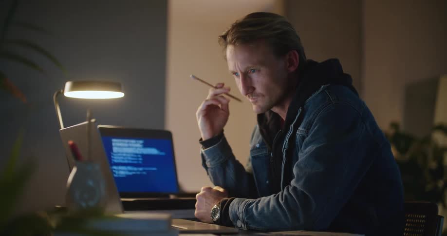 Man smiles and consults one computer before typing on a second computer